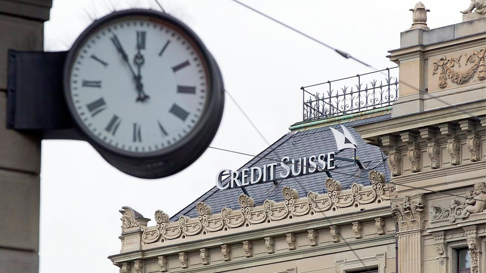 Uhr, die fünf vor zwölf zeigt, im Hintergrund Credit-Suisse-Logo auf Hausdach.