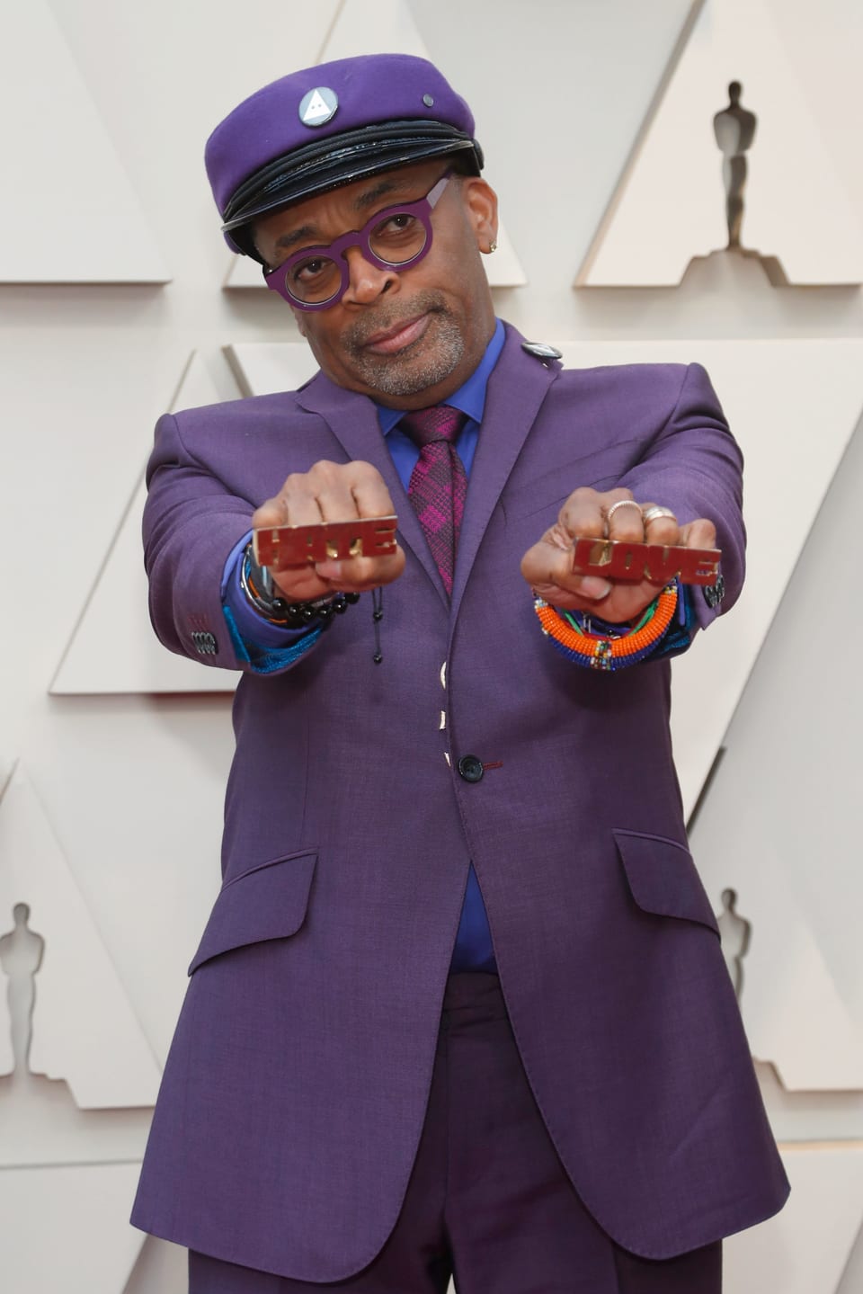 Spike Lee in einem violetten Anzug, der zwei Ringe mit «Hate» und «Love» in die Kamera streckt