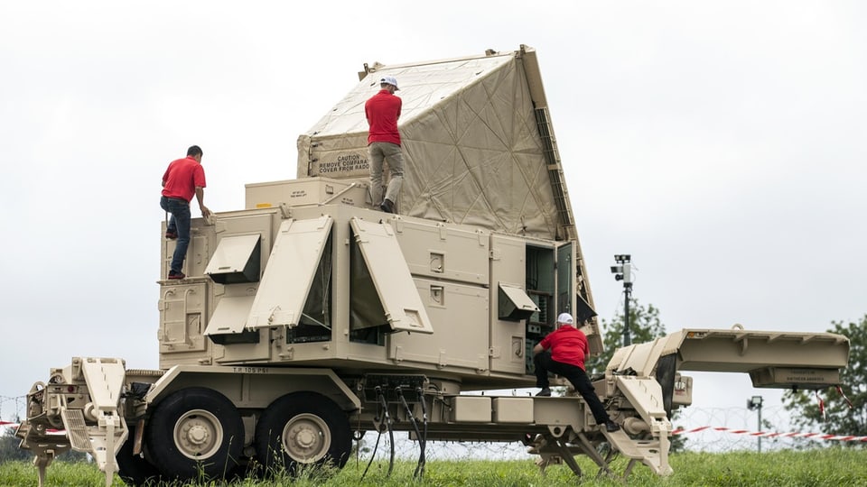 Drei Personen in roten Hemden arbeiten an einem Militärfahrzeug mit Radar.