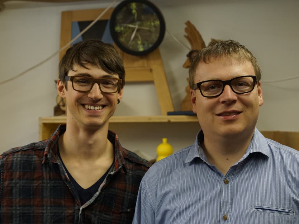 Zwei Männer mit Holzbrillen in einem Schreineratelier.