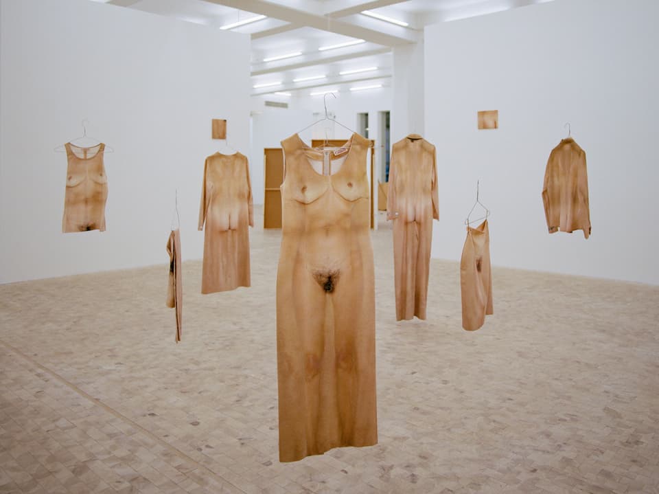 Nackte Körper auf Kleidung gedruckt hängen in einer Ausstellung von der Decke.