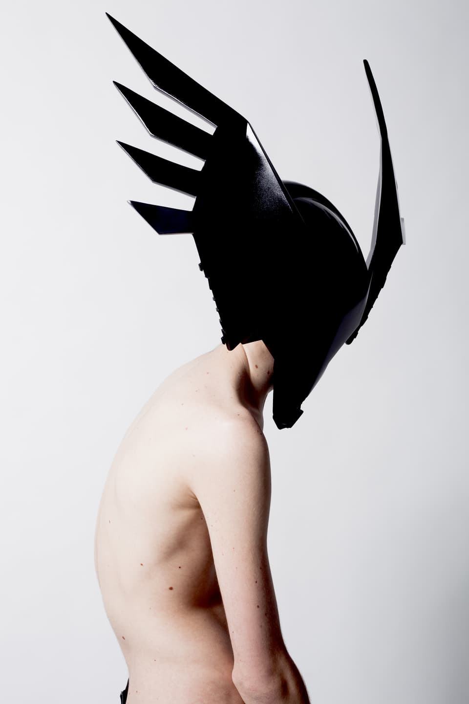 Die Ansicht eines nackten Menschen, der auf dem Kopf eine schwarze, glänzende Maske trägt.
