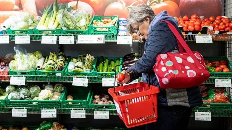 Frau mit Einkaufskorb vor Gemüseregal