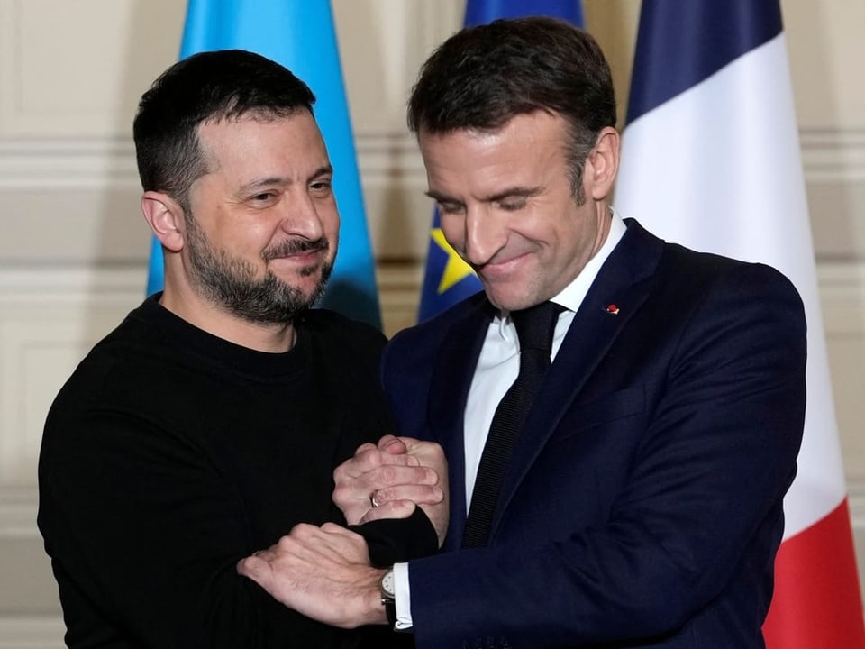 Macron und Selenski gegen sich scheinbar freundschaftlich die Hand. 