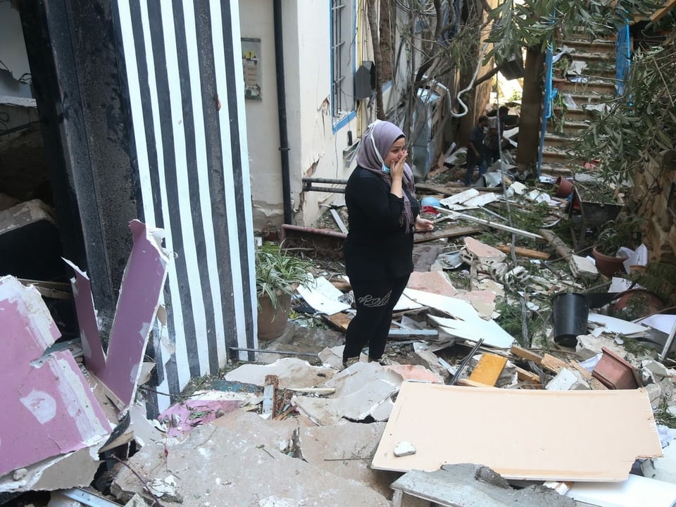 Eine Frau betrachtet die Zerstörung um sie herum verzweifelt, überall liegen Trümmerteile.