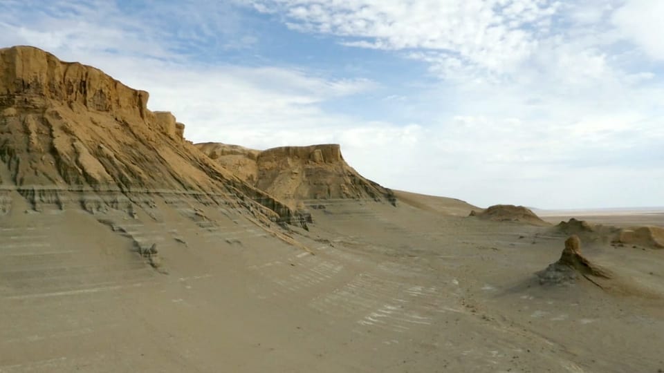 Eine Landschaftsaufnahme der Atacama-Wüste in Südamerika zeigt eine braun-sandige Ebene und Felsen im Hintergrund.