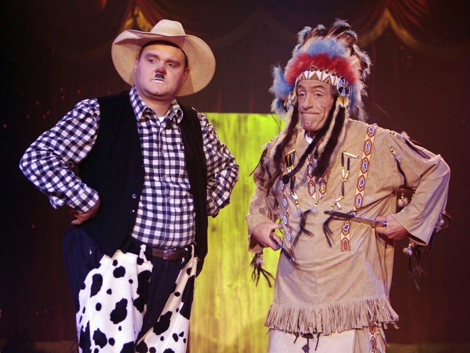 Ein Mann im Cowboy-Kostüm und ein Mann im Indianer-Kostüm.
