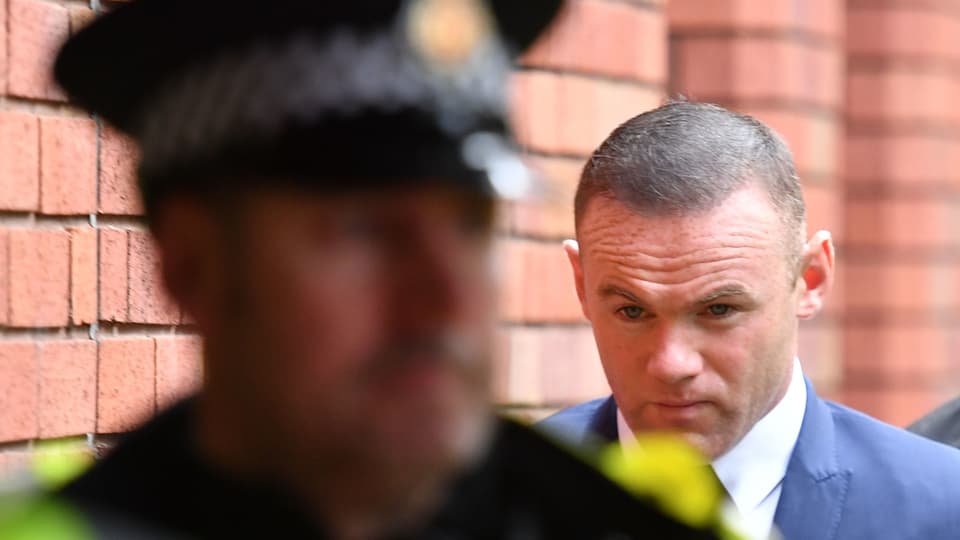 Wayne Rooney läuft mit nachdenklicher Miene hinter einem Polizisten her