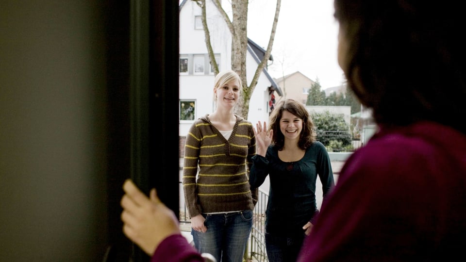 Eine Frau öffnet eine Tür, zwei Mädchen winken ihr.