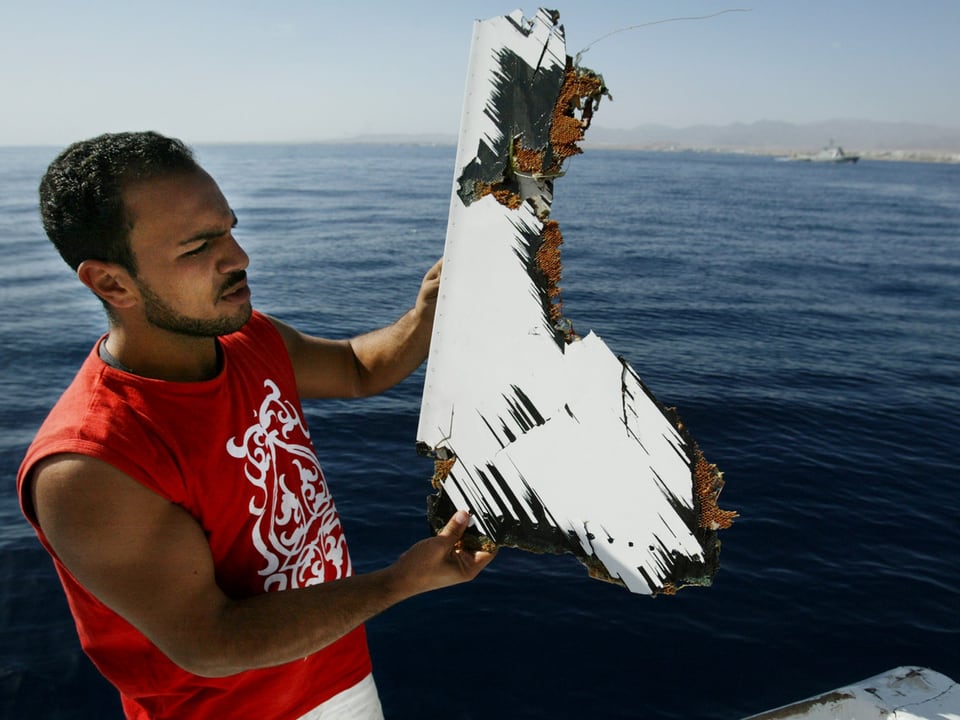 Ein Mann auf einem Schiff zeigt ein Stück des Flugzeugs, das ins Rote Meer stürzte. 