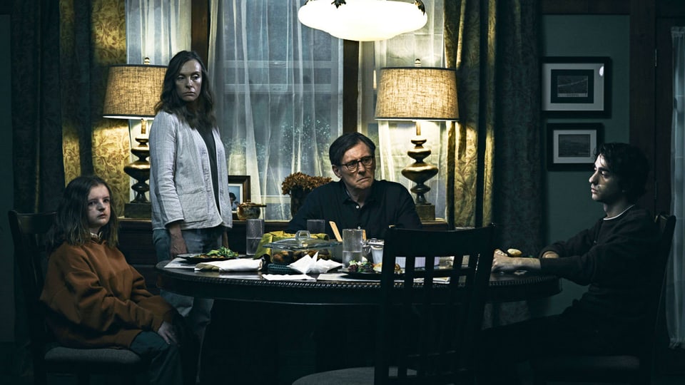 Eine Familie sitzt in einem düsteren Wohnzimmer um den Tisch