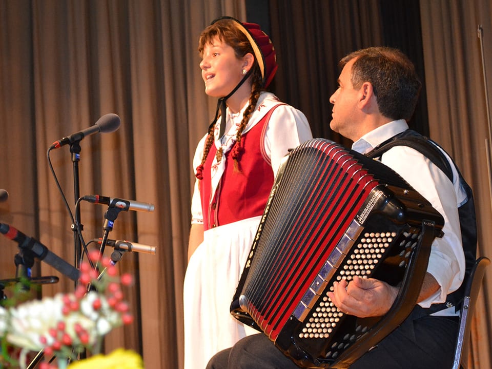 Eine junge Jodlerin wird von einem Akkordeonisten begleitet.