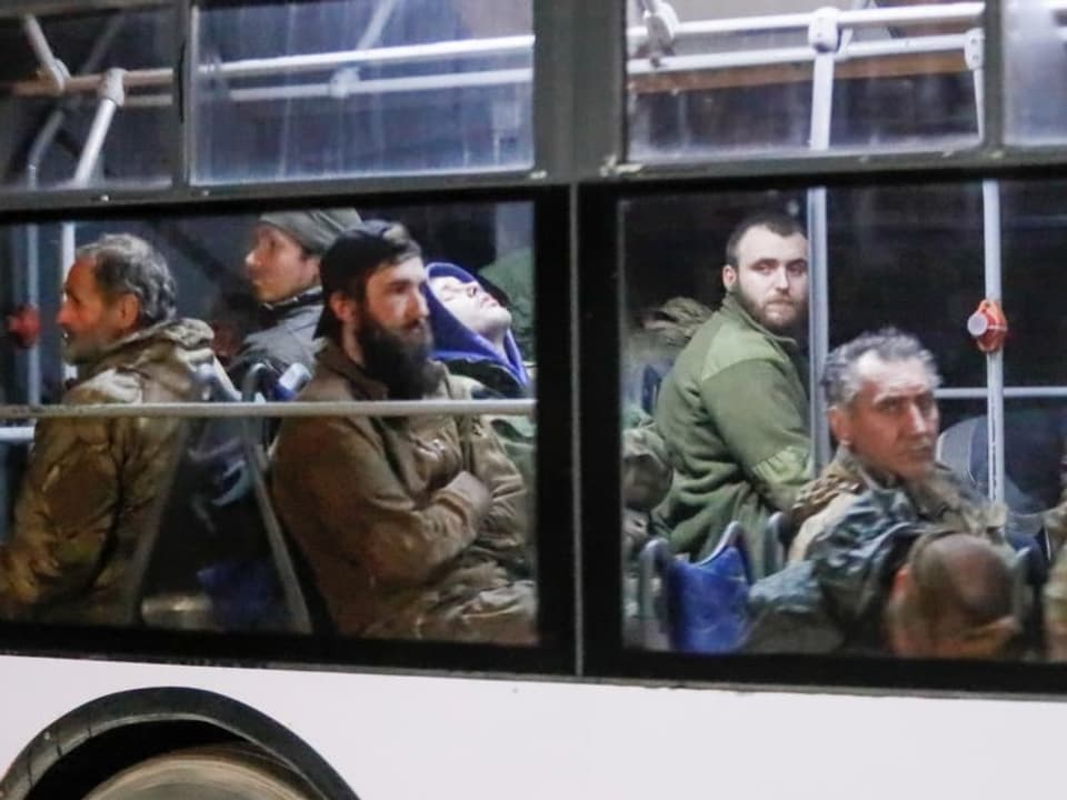 Männer in militär-grüner Kleidung sitzen in einem Bus.