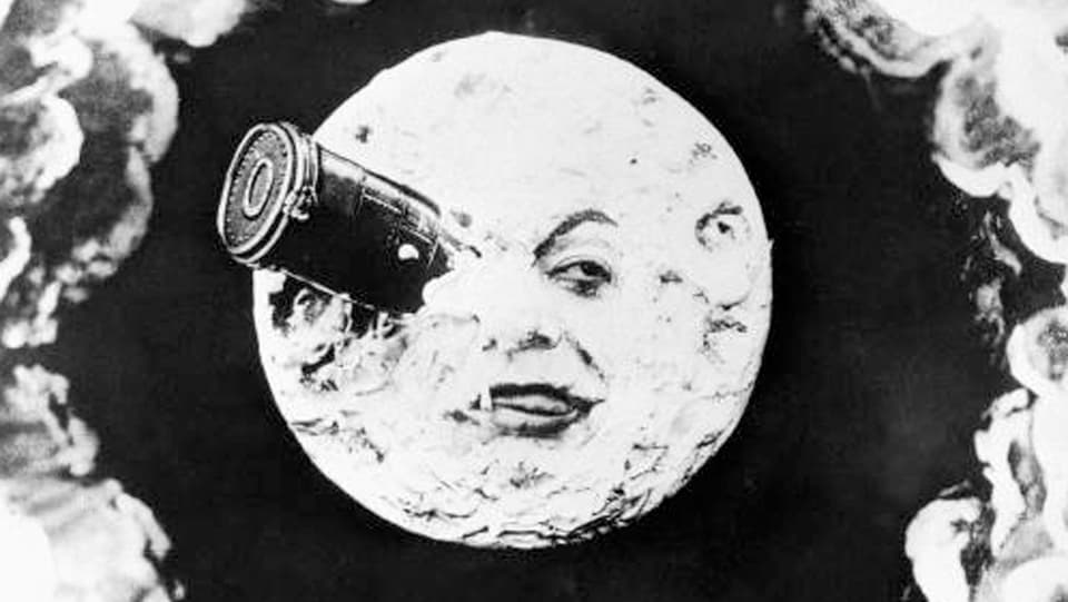 Schwarz-Weiss-Bild: Ein Mond mit einem Gesicht. Ein Auge ist von einem Fernrohr bedeckt.