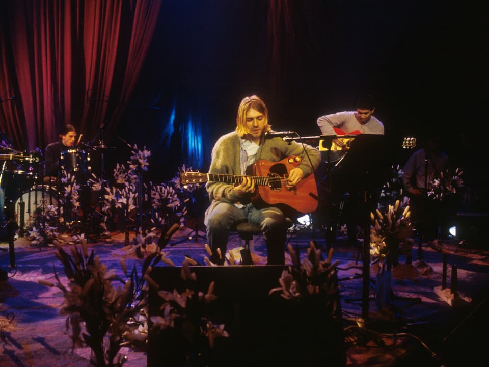 Kurt Cobain sitzt mit Gitarre auf der Bügne