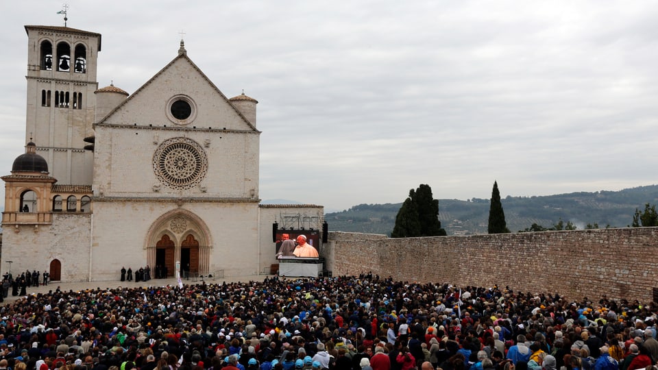 Menschen verfolgen vor der Basilika San Francesco in Assisi die Predigt des Papstes auf einem Bildschirm.