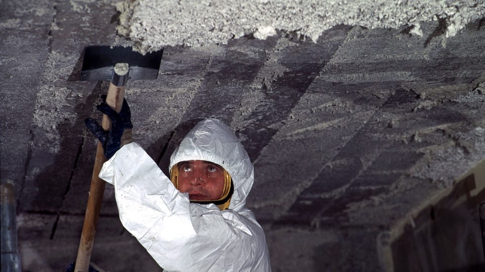 Arbeiter mit Schutzanzug kratzt Asbest von einer Decke.