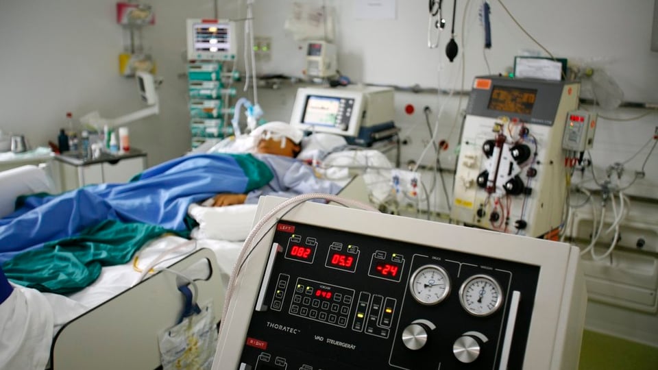 Person in Krankenbett, an Geräte angeschlossen