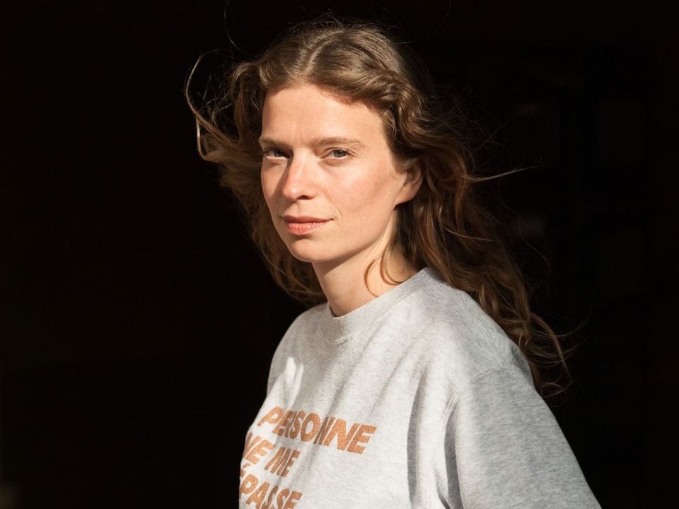 Frau mit langen Haaren und Pullover vor dunklem Hintergrund.