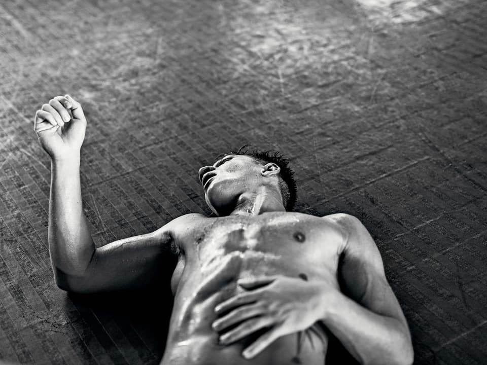 Schwarzweissbild eines Mannes mit nacktem Oberkörper, der erschöpft am Boden liegt