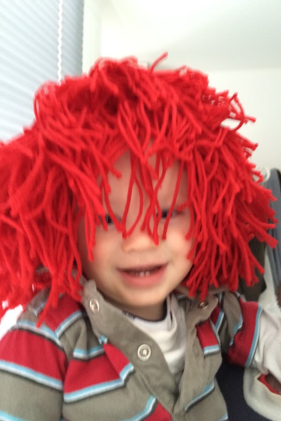 Kind mit roter Kappe aus hängenden Wollfäden.