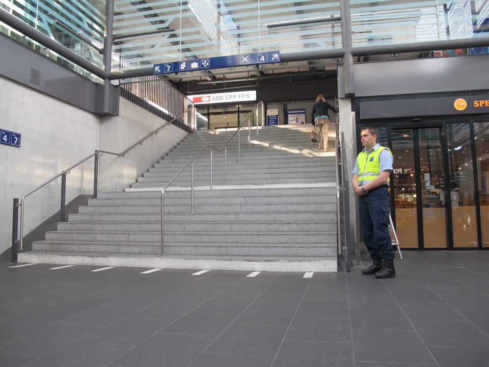 Securitas-Mitarbeiter in gelber Weste wartet unten an der Treppe. 