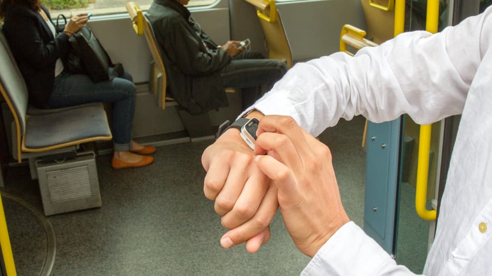 Im Tram mit der Uhr, im Hintergrund zwei Personen, die auf ihrem Smartphone herumtippen.