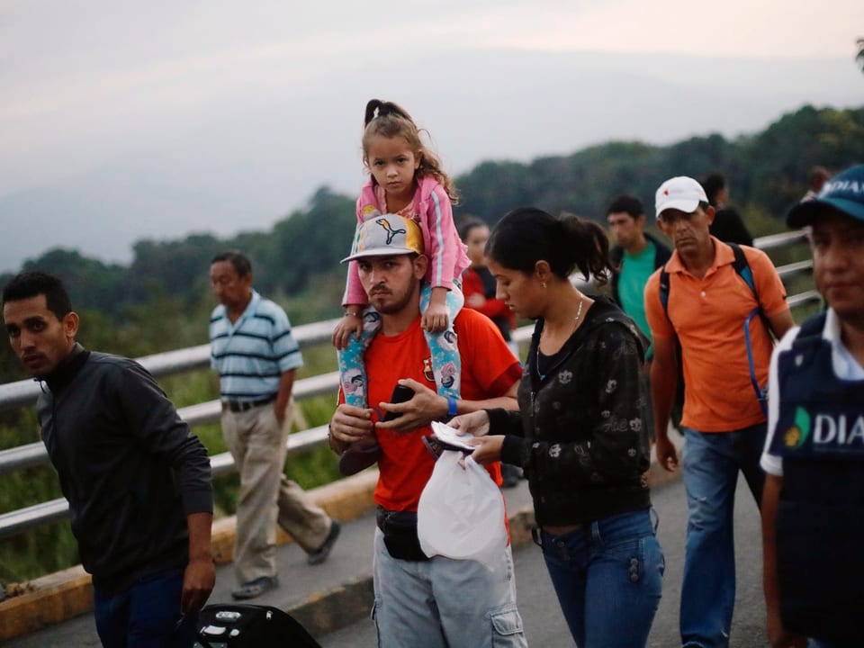 Eine kleinere Gruppe von venezolanischen Flüchtlingen läuft neben einem Brückengeländer. Ein Mann trägt ein Mädchen auf der Schulter.