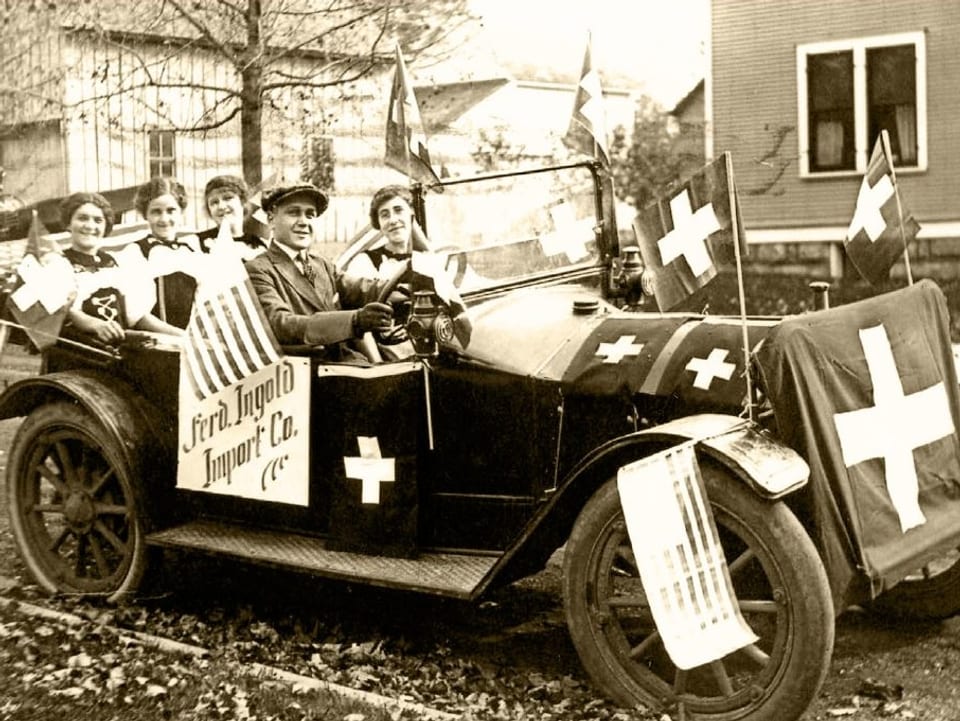 Ein Archivbild: Personen in einem alten Auto mit Schweizer Flaggen