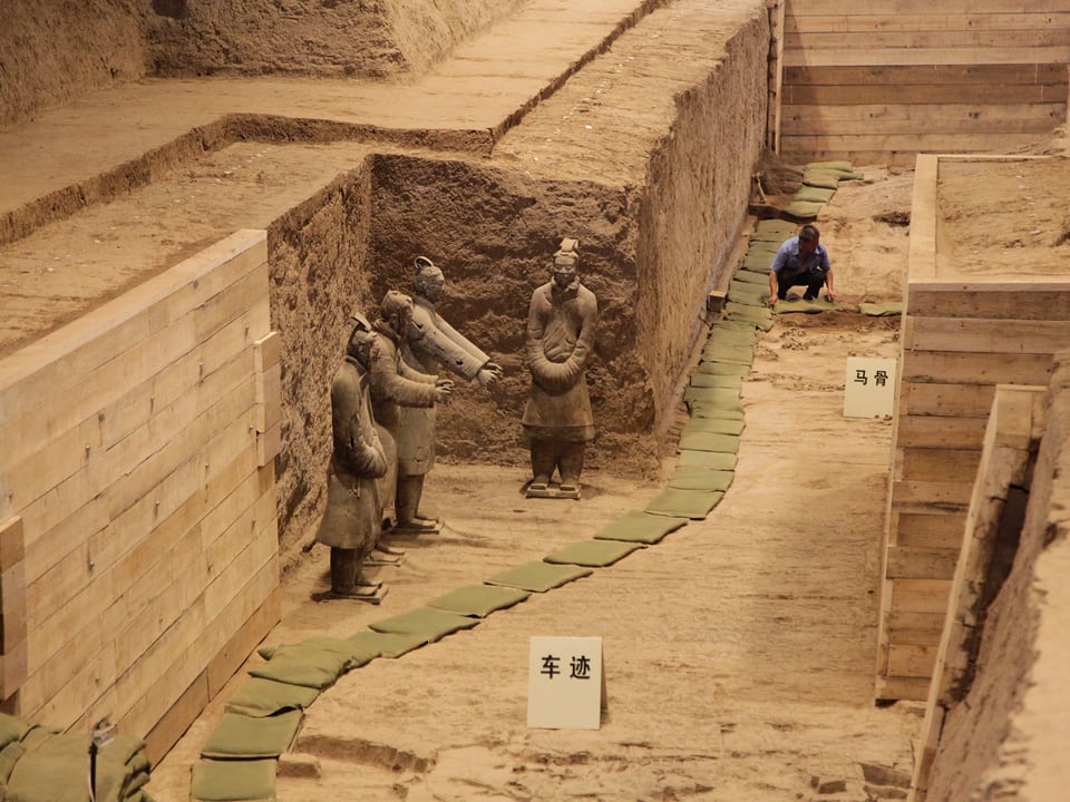 Ein Mann in der Ausgrabungsstätte, vier Figuren stehen freigelegt da.