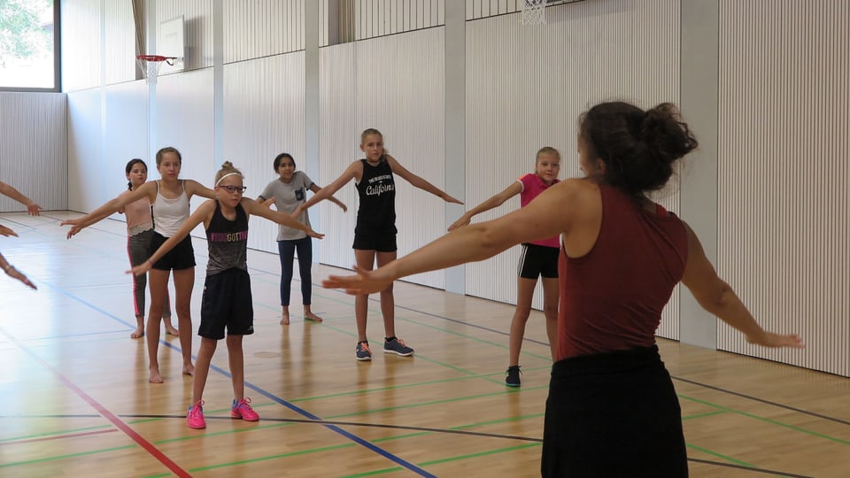 Eine Tanzlehrerin zeigt Mädchen in einer Turnhalle vor, was sie tanzen sollen.