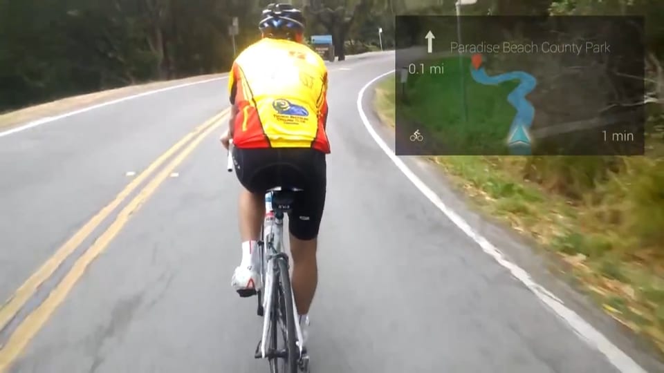 Blick durch ein Google Glass: Eine Strasse mit Radfahrer, in der oberen rechten Ecke wird eine Strassenkarte eingeblendet