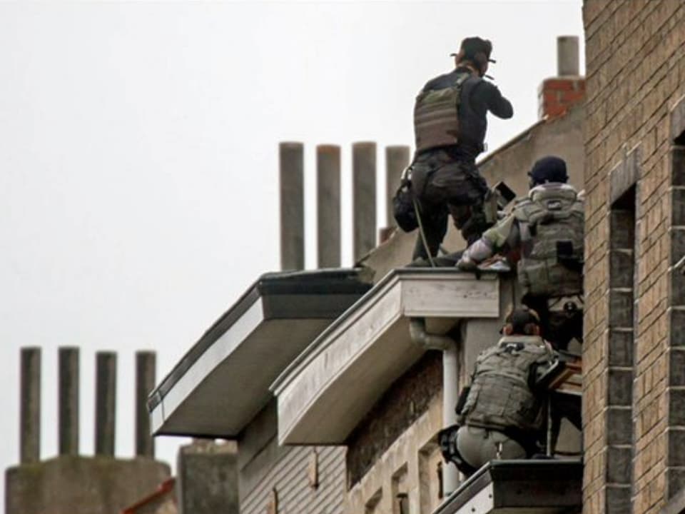 Drei Polizeibeamte begeben sich mit der Waffe im Anschlag auf ein Dach