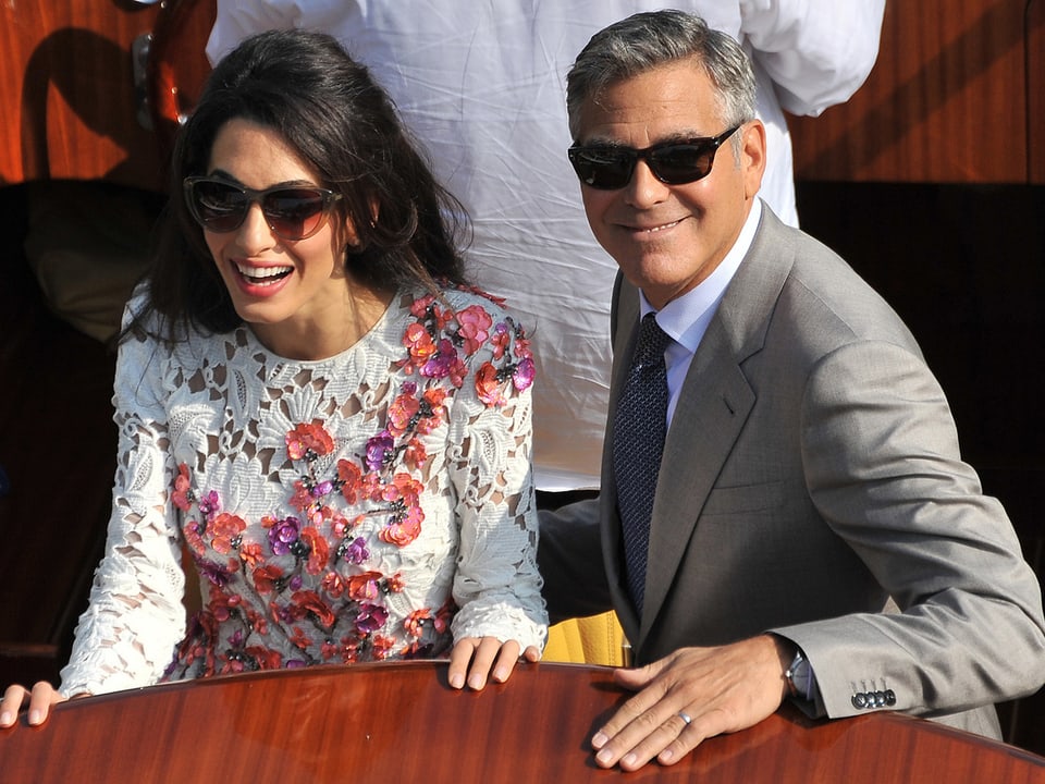 Amal Alamuddin (links) und George Clooney lächeln nebeneinander stehend auf einem Boot