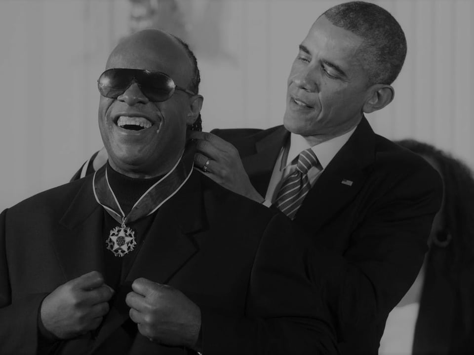Schwarz-weiss-Bild von Wonder und Obama. Obama bindet Stevie Wonder gerade die Medallie um den Hals.