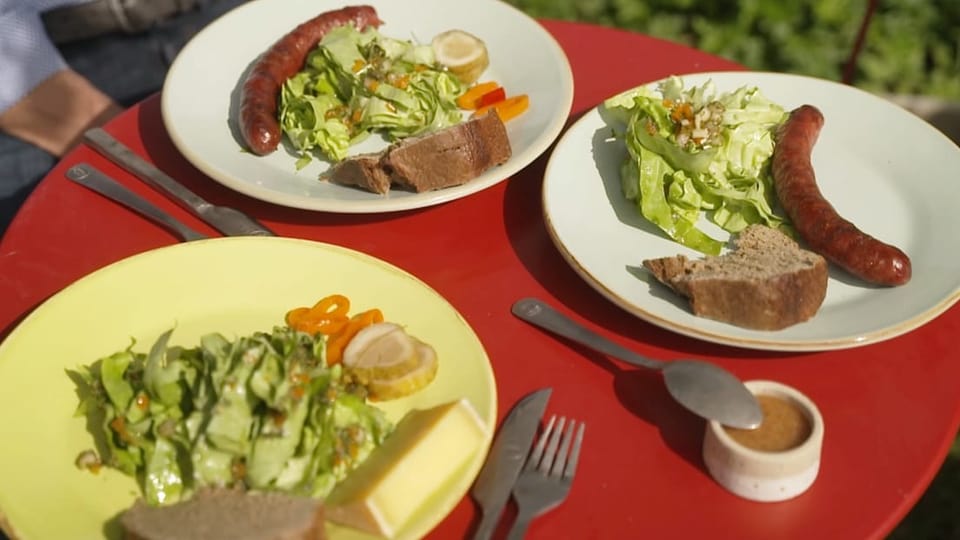 Teller mit Wurst und Salat auf rotem Tisch