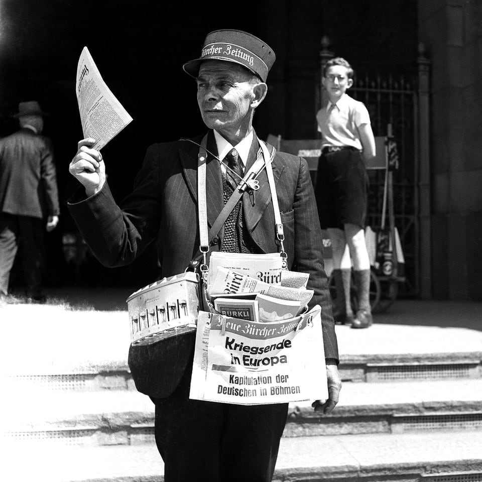 Ein Zeitungsverkäufer hält die NZZ in der Hand.