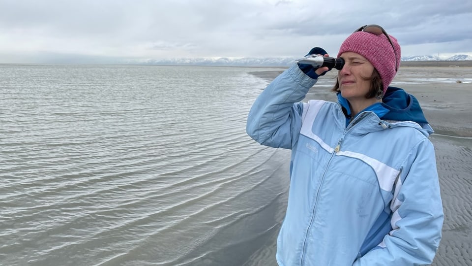 Frau in hellblauer Jacke schaut durch Rohr am Ufer des Salt Lake