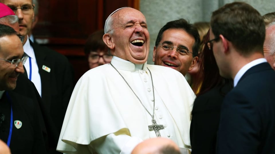 Der Papst in weissem Gewand, umgeben von zahlreichen Männern, lacht.