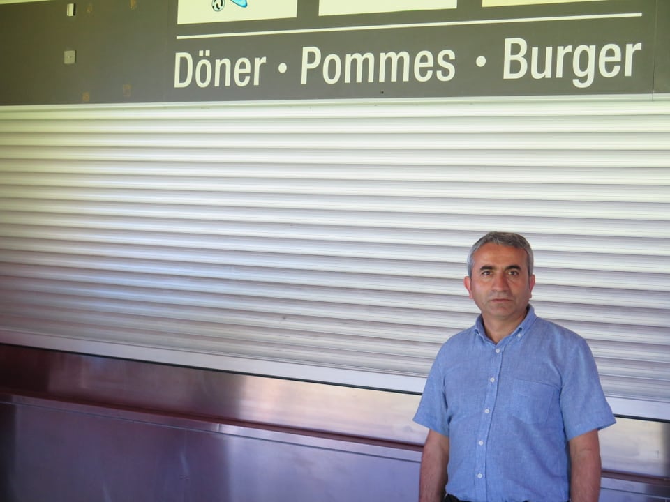 Atici steht vor einem geschlossenen Stand, oben steht Döner, Pommes, Burger. 