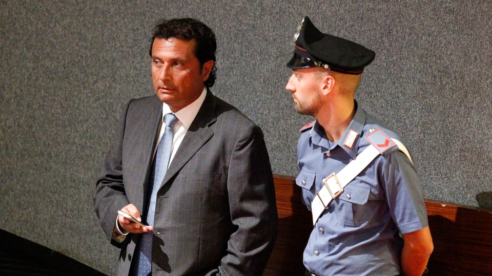 Kapitän Schettino steht neben einem Polizisten im Gericht von Grossetto.
