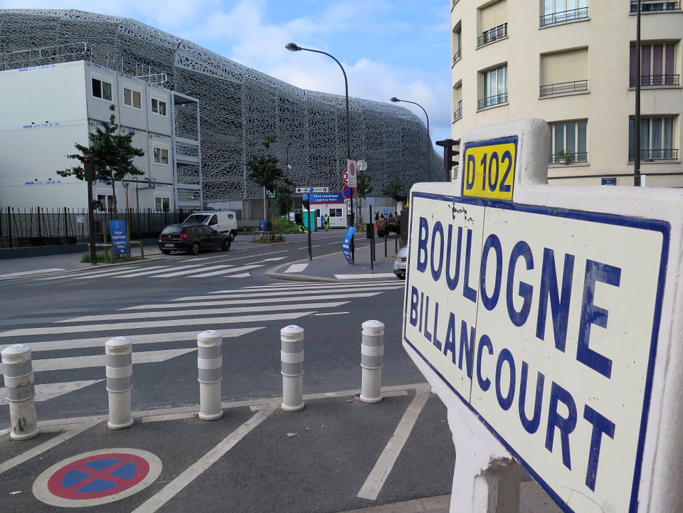Strassenaufnahme, auf der rechten Seite ist ein Strassenschild erkennbar. Darauf steht: «Boulogne Billancourt»