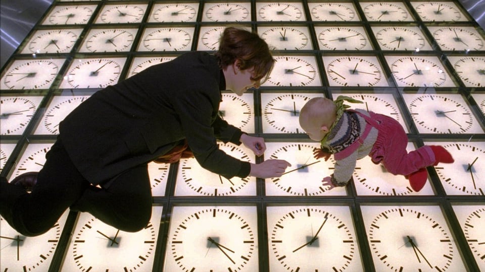 Eine Frau und ein Baby hocken auf einer Installation in einem Museum bestehend aus Uhren