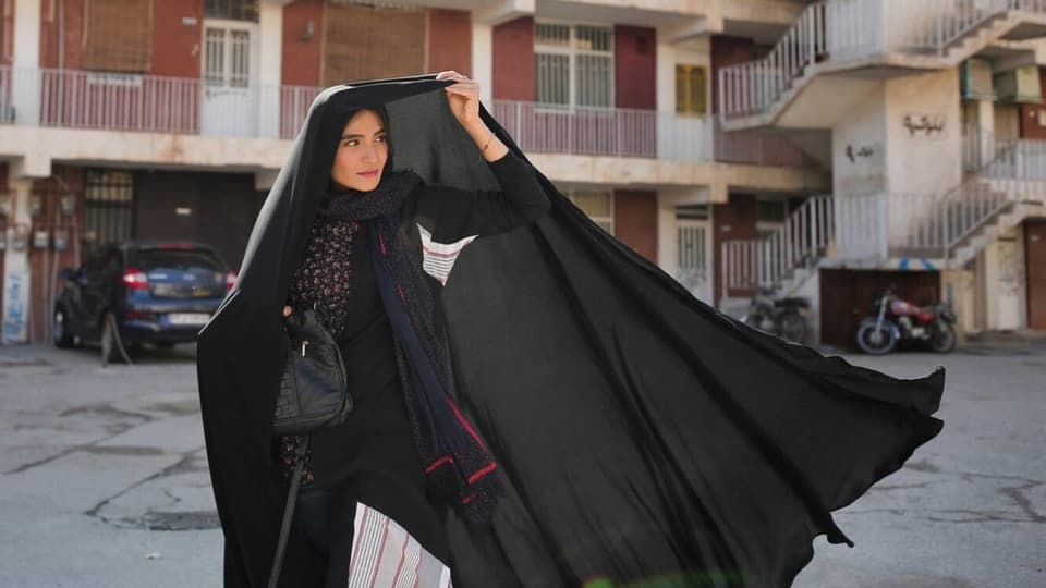Woman with a headscarf under a black sheet.