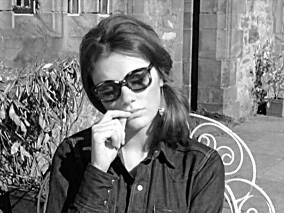 Eine Frau mit Sonnenbrille sitzt auf einem Gartenstuhl und wirkt in sich gekehrt.