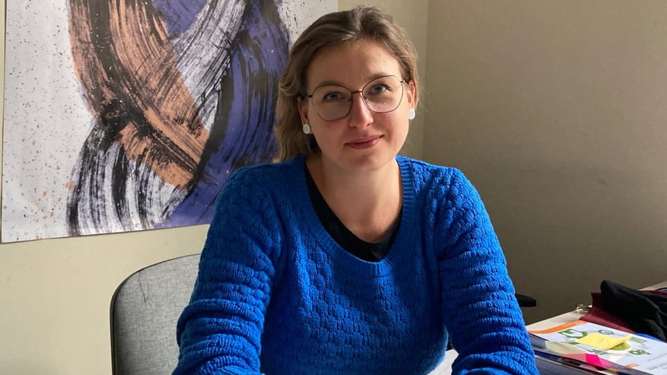 Katarzyna Komar-Macyńska trägt einen blauen Pullover und eine Brille. Sie sitzt in ihrem Büro an einem Tisch. 