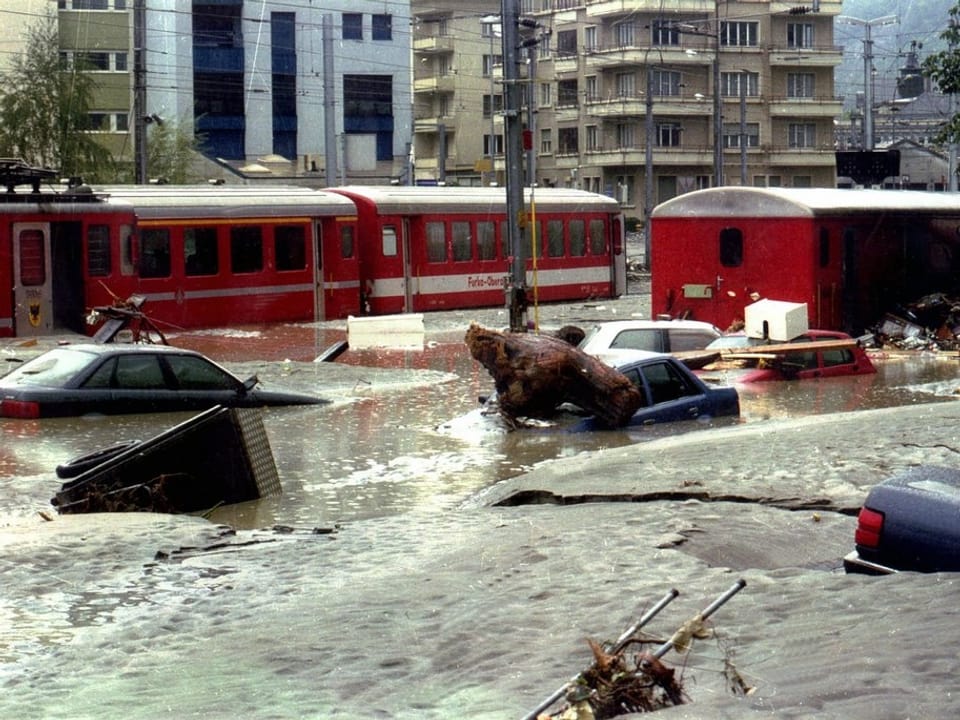 Autos und Züge versinken auf dem Bahnhofplatz im Schlamm.