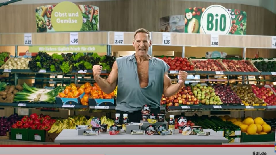 Mann mit offenem Hemd steht vor Gemüseregal 