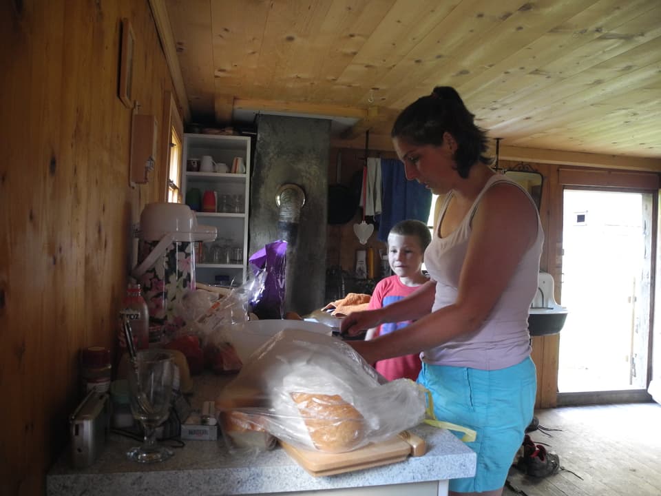Frau wird von Sohn dabei beobachtet, wie sie auf Küchentheke Essen zubereitet.