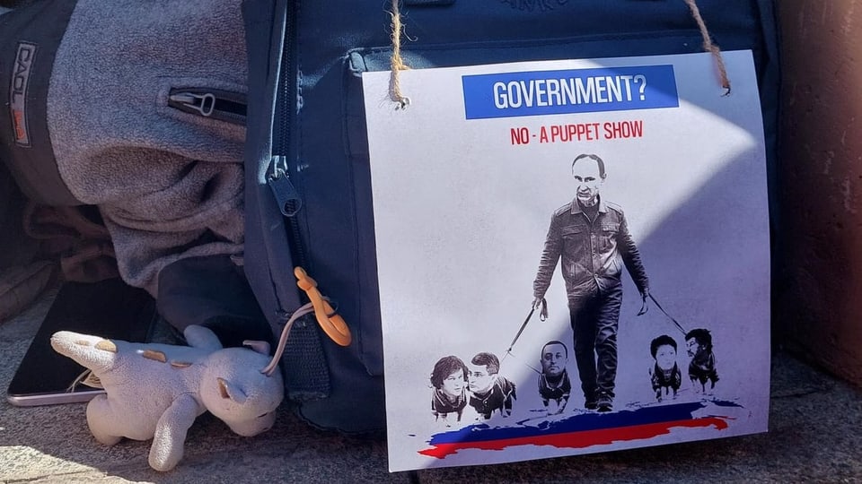Ein Plakat zeigt Putin, der mit vier Personen (mit Menschenköpfen und Hunde-Unterleib) an der Leine Gassi geht.